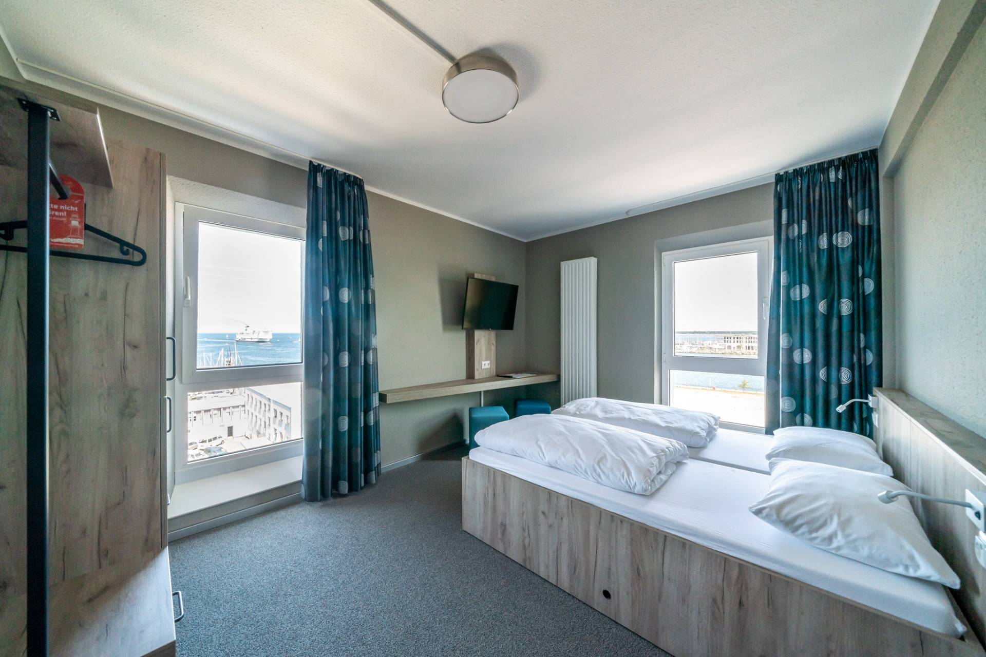Helles Doppelzimmer des WIROtels mit zwei Fenstern, Bett, Schreibtisch und Fernseher