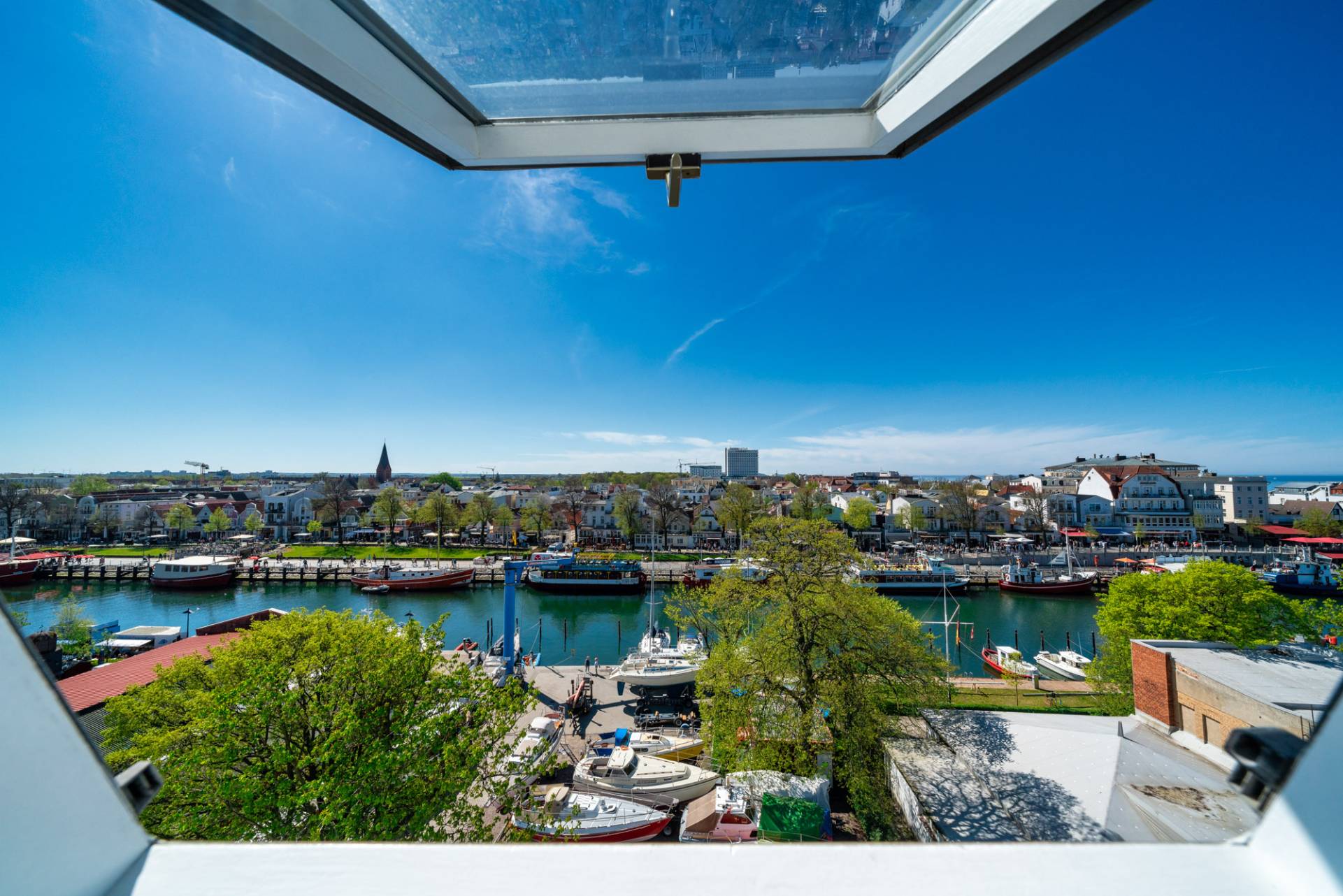 Blick durch ein geöffnetes Dachfenster des WIROtels auf den Alten Strom und Warnemünde