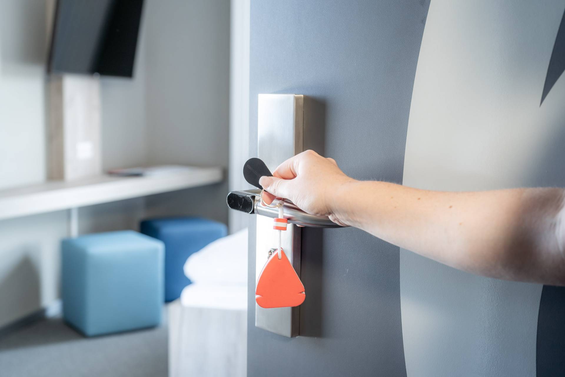 Hand öffnet eine Zimmertür mit elektronischem Türschloss und rotem Schlüsselanhänger