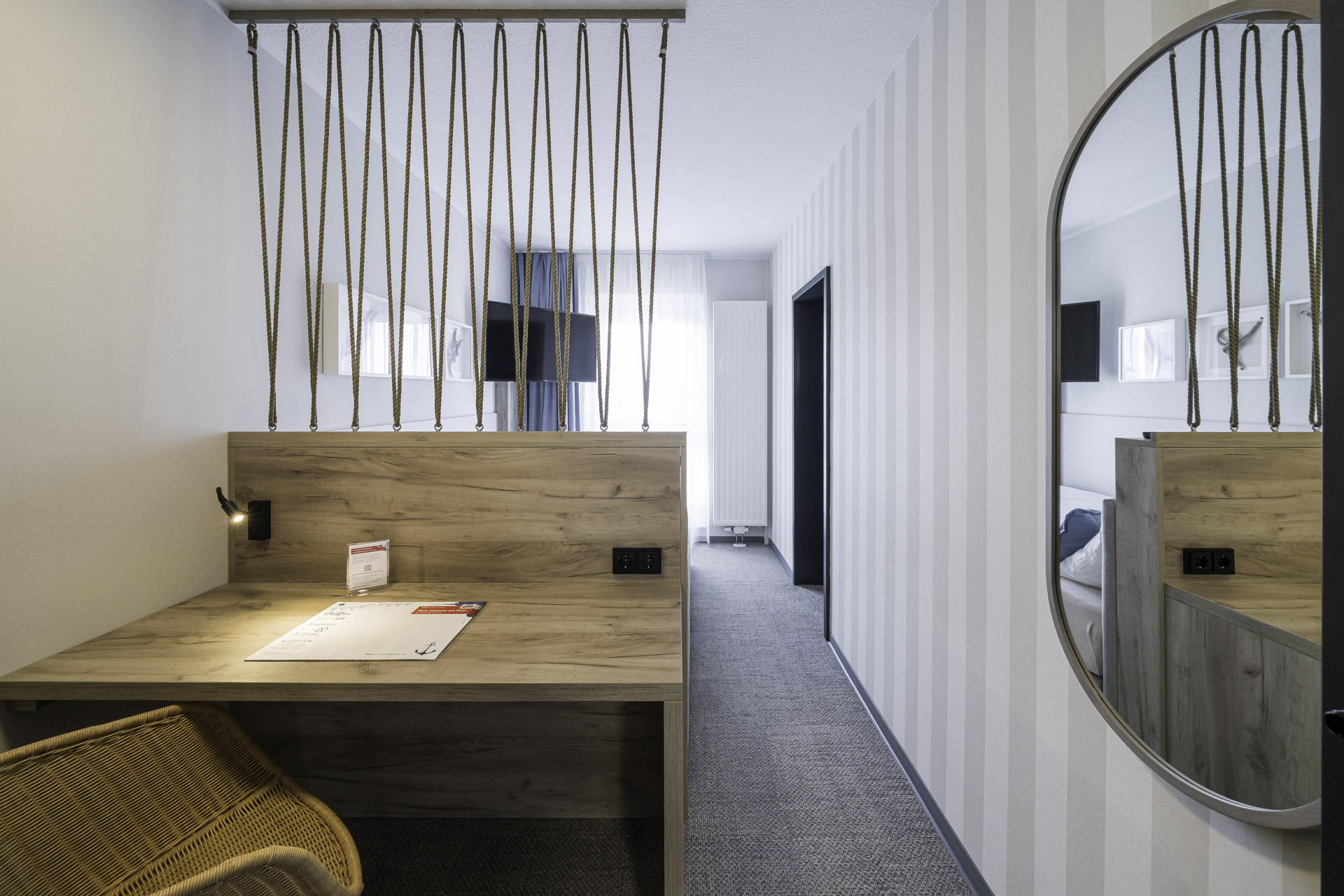 Kleines Doppelzimmer des WIROtels mit Schreibtisch, Fernseher und offenem Raumteiler zum Bett