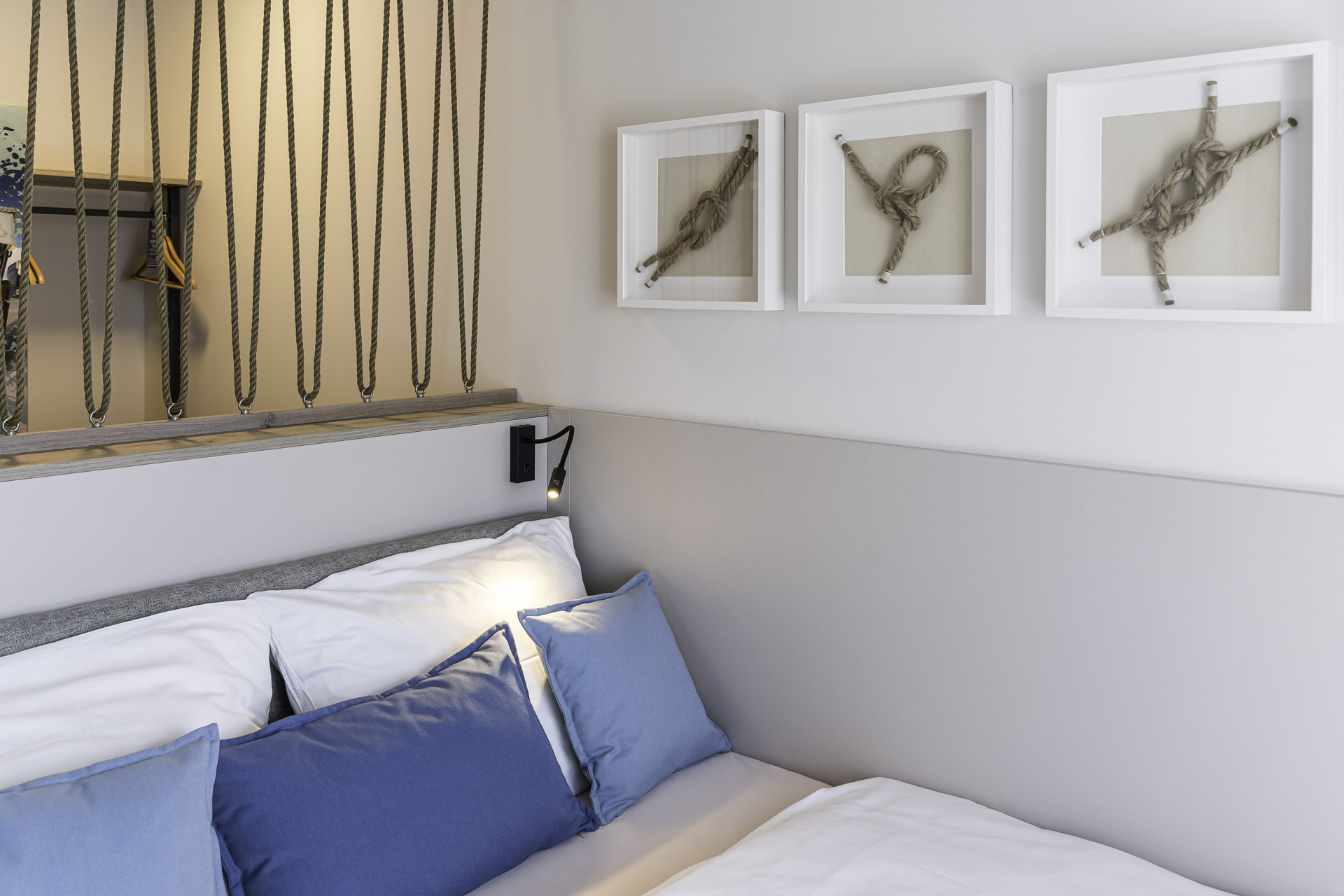 Bett im kleinen Doppelzimmer mit blauen Kissen und gerahmten Bildern an der Wand