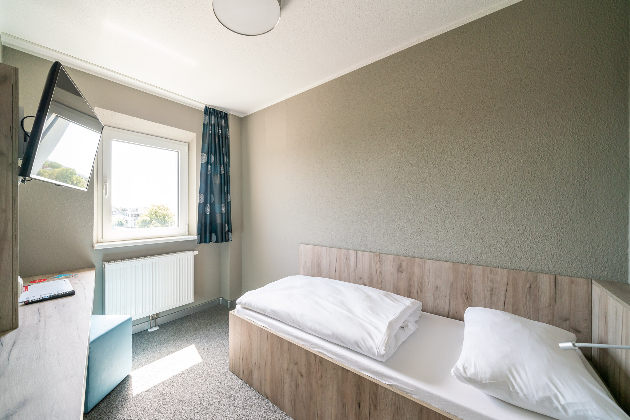 Einzelzimmer des WIROtels mit Einzelbett, Fenster und kleinem Sitzbereich